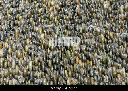 Closeup of water flowing over rounded multicolored river rocks background Stock Photo