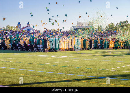 Ground level view of the culmination of a high school graduation taking place on a football field while students toss their caps Stock Photo