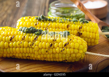 Homemade grilled corn on cob with pesto sauce on wooden board Stock Photo