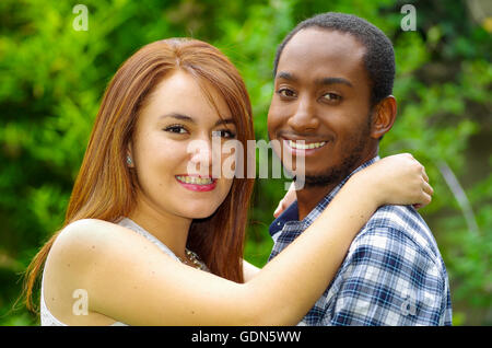 Interracial charming couple wearing casual clothes embracing and posing for camera in outdoors environment Stock Photo