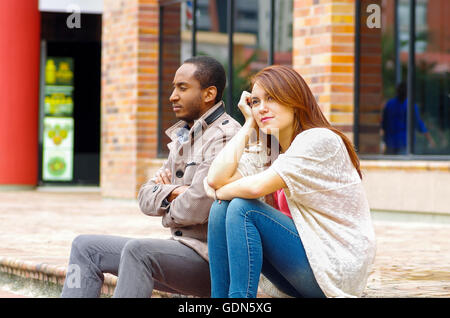 Interracial upset couple sitting on steps in front of building, simulating argument for camera Stock Photo
