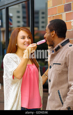 Interracial charming couple wearing casual clothes interacting happily and sharing an ice cream Stock Photo