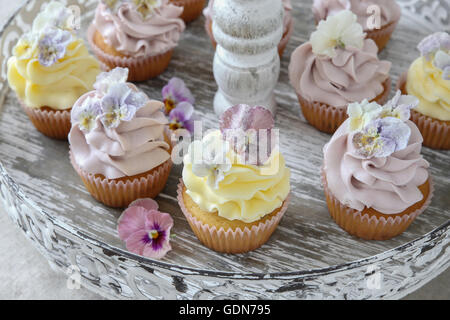 Purple and yellow cupcakes with sugared edible flowers on vintage cake stand Stock Photo