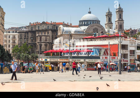 Istanbul, Turkey - July 1, 2016: Ordinary people walk on Taksim square. Cityscape of Istanbul with Hagia Triada church on a back Stock Photo