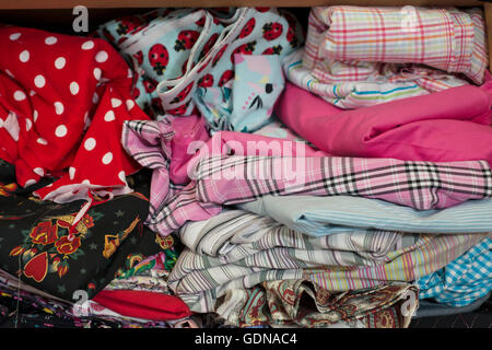 A pile of textile or cloth of various colours and designs in wooden shelving. Stock Photo