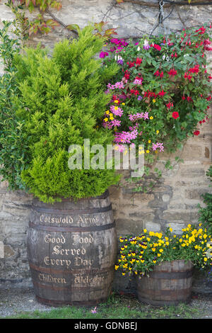 Beer barrel planters and a hanging basket with floral displays outside The Cotswolds Arms pub, Burford, Oxfordshire, England Stock Photo