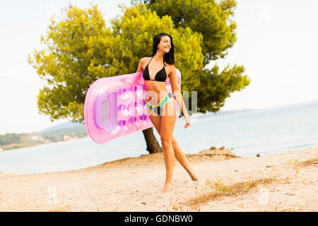 Pretty young woman holding an air mattress on the beach at summer Stock Photo