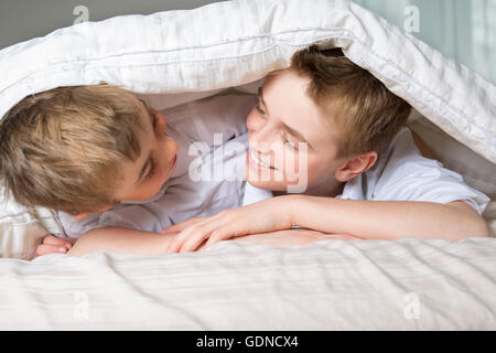 boy hiding in bed under a white blanket or coverlet. Stock Photo