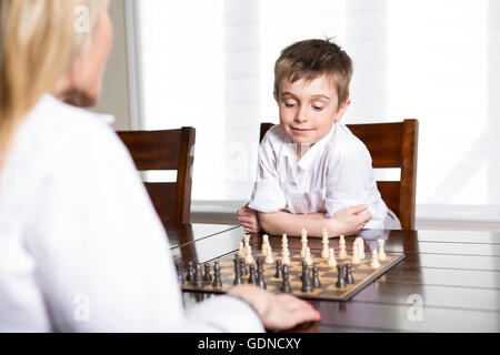 boy playing chess at home with mother Stock Photo
