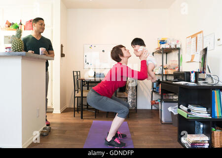 Father watching mother doing squats with baby in arms Stock Photo