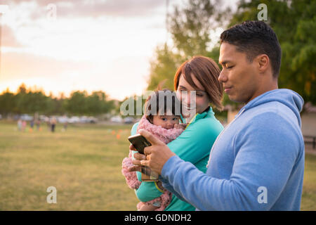 Couple with baby, using mobile phone in park Stock Photo
