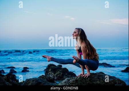 Young woman practicing yoga pose on rocks at beach, Los Angeles, California, USA Stock Photo