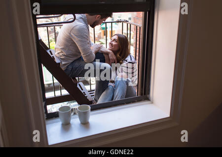 Young couple sitting on fire escape, smiling Stock Photo