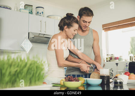 Young woman helping boyfriend to slice wholemeal bread at kitchen counter Stock Photo