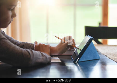 Girl at desk using pencil as stylus on digital tablet Stock Photo