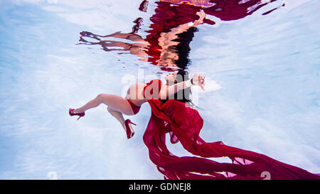Pregnant woman wearing red high heels and bikini in swimming pool Stock Photo