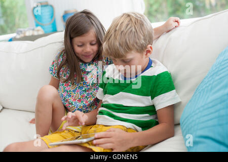 Brother and sister on sofa using digital tablet Stock Photo