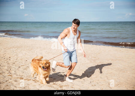 Smiling handsome young man jogging with his dog on the beach Stock Photo