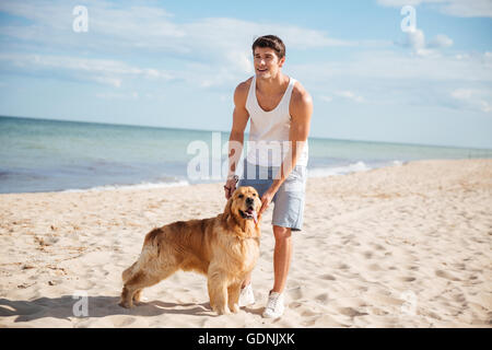 Happy attractive young man walking and playing with his dog on the beach Stock Photo