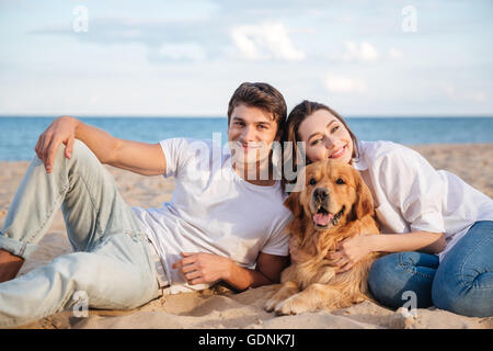 Happy young couple with their dog lying and relaxing on the beach Stock Photo