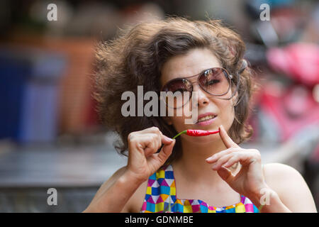 Asian young woman with a small red pepper in hand, close-up portrait in the market. Stock Photo