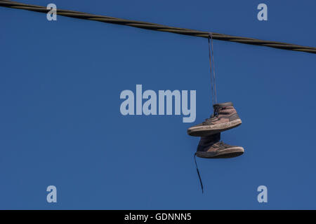 Boots hanging from overhead cable - representing the 'Territorial' concept of drugs, drug dealing turf, & associated addiction, gangland, shoe tossing Stock Photo