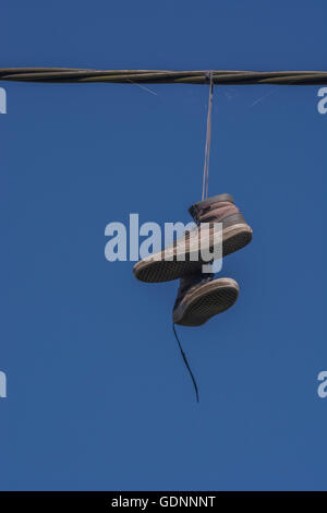 Boots hanging from overhead cable - representing the 'Territorial' concept of drugs, drug dealing turf, & associated addiction, gangland, shoe tossing Stock Photo