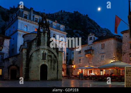 St. Luke's Church in the square (Trg Sv Luke) and the city fortifications above on a moonlit evening: Kotor, Montenegro Stock Photo