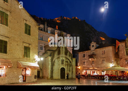 St. Luke's Church in the square (Trg Sv Luke) and the city fortifications above on a moonlit evening: Kotor, Montenegro Stock Photo