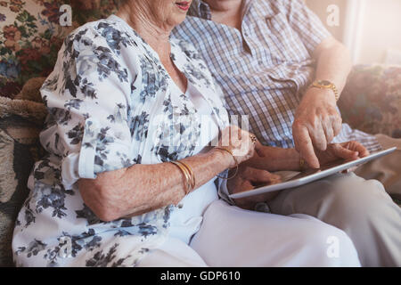 Cropped shot of senior couple sitting together using touch screen computer. Focus on hands of elderly couple and digital tablet. Stock Photo