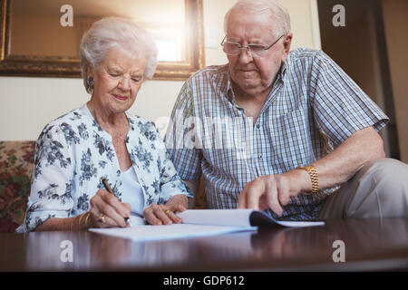 Indoor shot of mature couple at home signing documents together. Senior man and woman sitting on sofa doing retirement paperwork Stock Photo