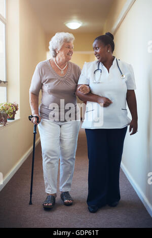 Senior woman with walking stick being helped by female nurse at home. Full length shot of female doctor supporting elderly patie Stock Photo