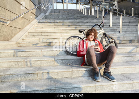 Man sitting on steps with BMX using smartphone Stock Photo