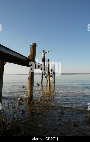 Woman on pier arms raised in yoga position Stock Photo