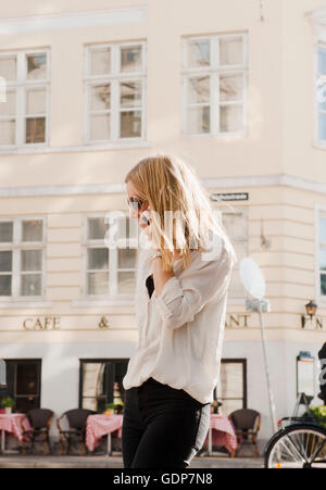 Woman using mobile phone opposite cafe, Copenhagen, Denmark Stock Photo