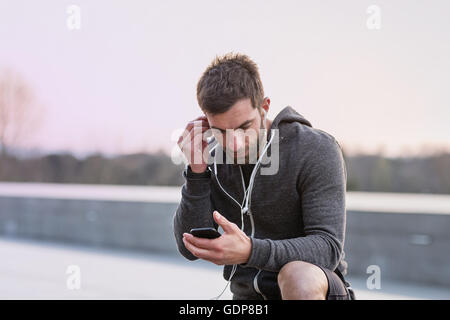 Mid adult man, outdoors, looking at smartphone, wearing earphones Stock Photo