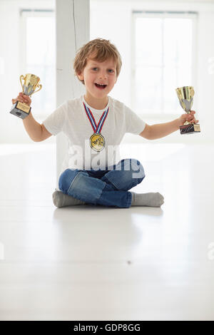 Portrait of boy wearing gold medal holding up trophies Stock Photo