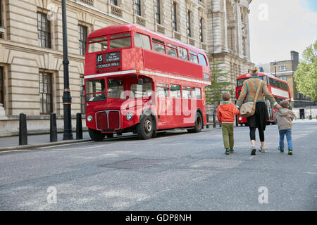 Rear view of mother and sons looking at red double decker bus Stock Photo