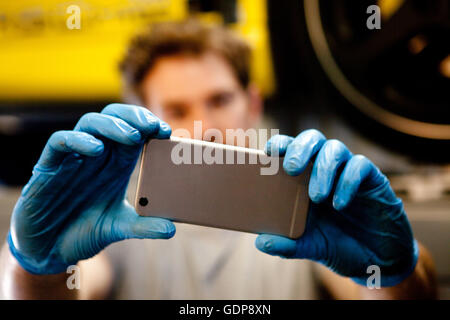 Male mechanic in workshop taking photo of car with mobile phone Stock Photo