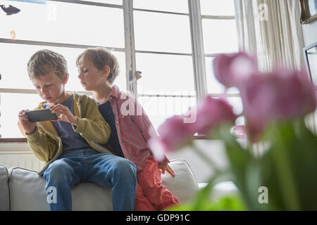 Boy sitting on sofa looking over brother shoulder at smartphone
