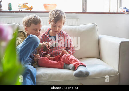 Boys sitting on sofa looking at smartphone Stock Photo