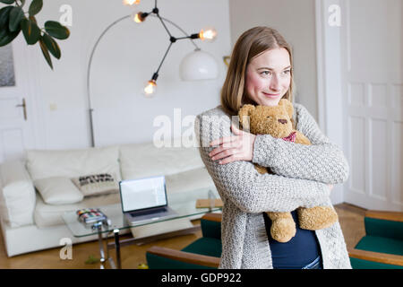 Mid adult woman hugging teddy bear in living room Stock Photo
