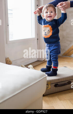 Baby boy holding mothers hands and standing on suitcase Stock Photo