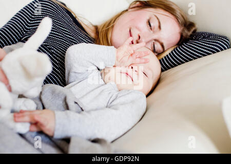 Tired baby girl and mother reclining on sofa Stock Photo