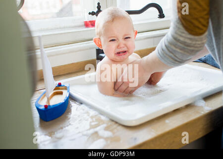 Mother removing upset baby son from kitchen sink Stock Photo