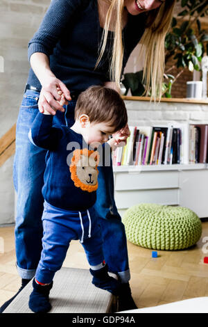 Mid adult woman taking first steps with baby son in living room Stock Photo