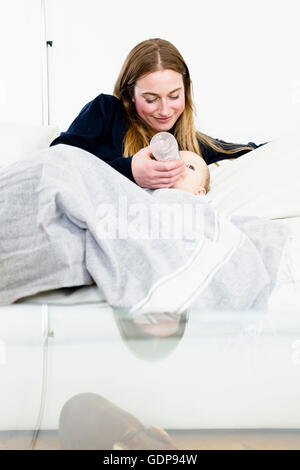 Mid adult woman feeding bottle to baby daughter on sofa Stock Photo