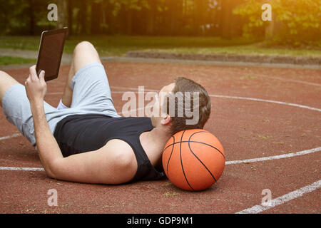 Young male basketball player lying on court browsing digital tablet Stock Photo