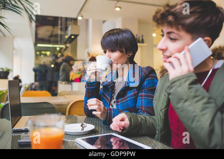 Two sisters in cafe using laptop, digital tablet and smartphone Stock Photo