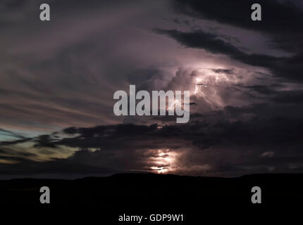 A powerful updraft ricochets off the stratosphere creating a large, expanding anvil cloud.  Lightning shoots out Stock Photo